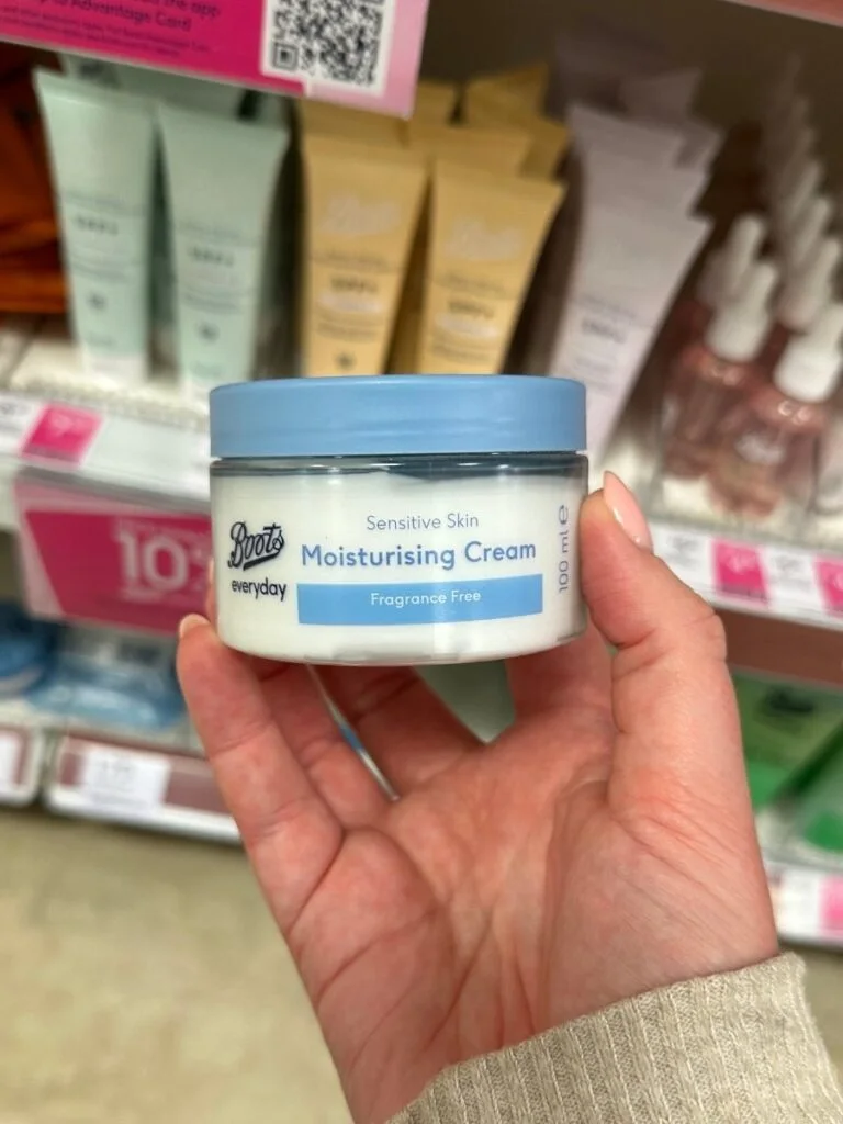 A hand holding a Boots own brand moisturising cream which is a great way to save money when shopping at Boots