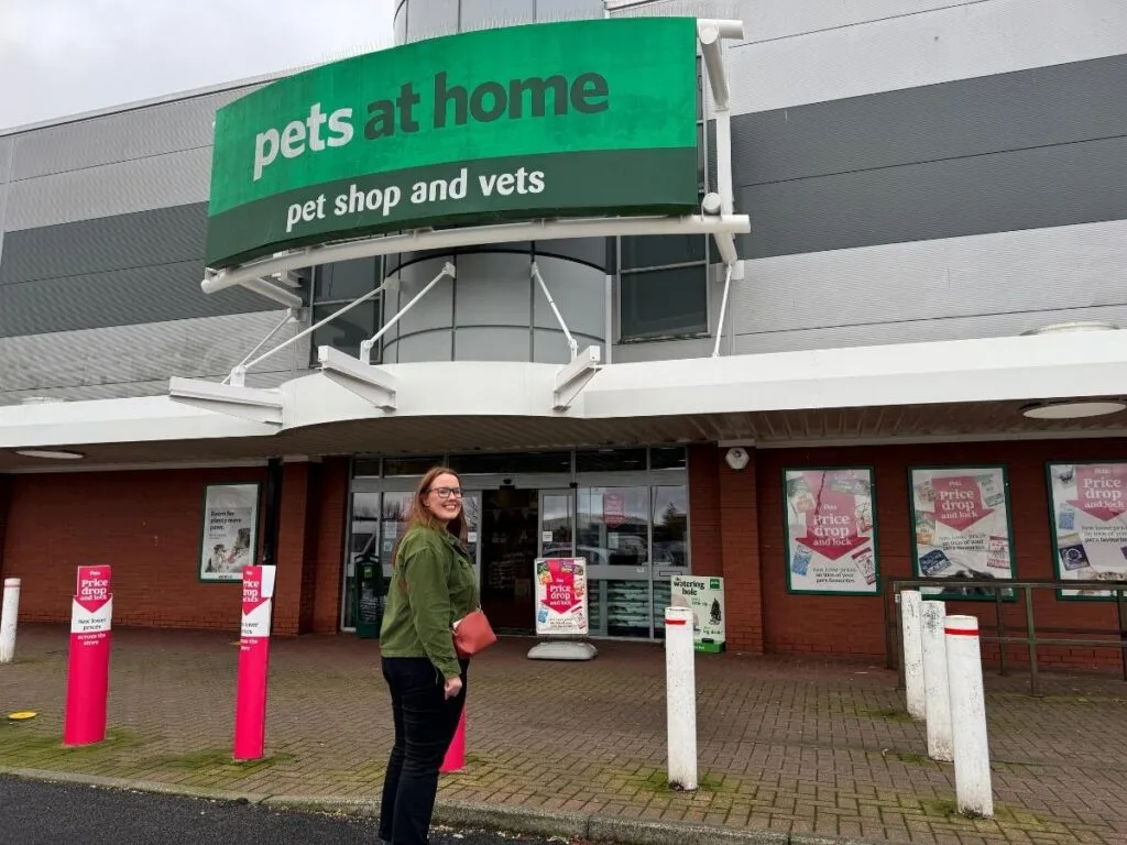 Chloe is standing outside of Pets at Home store and savings posters are displayed