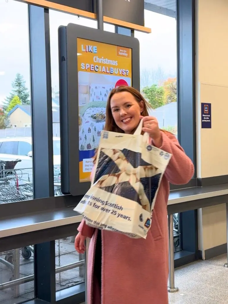 chloe smiling at the camera holding up a bag of shopping to show you how to save money at Aldi