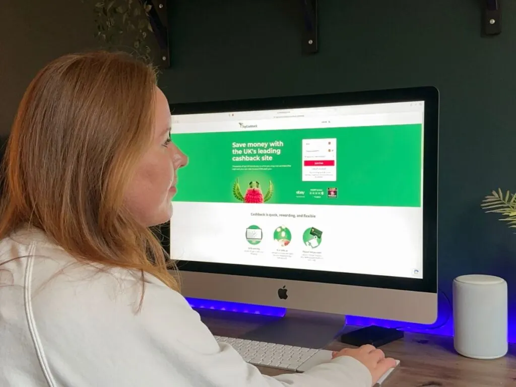 Chloe from Chloe's Deal Club sitting at a desk looking at a computer screen with TopCashback home page displayed