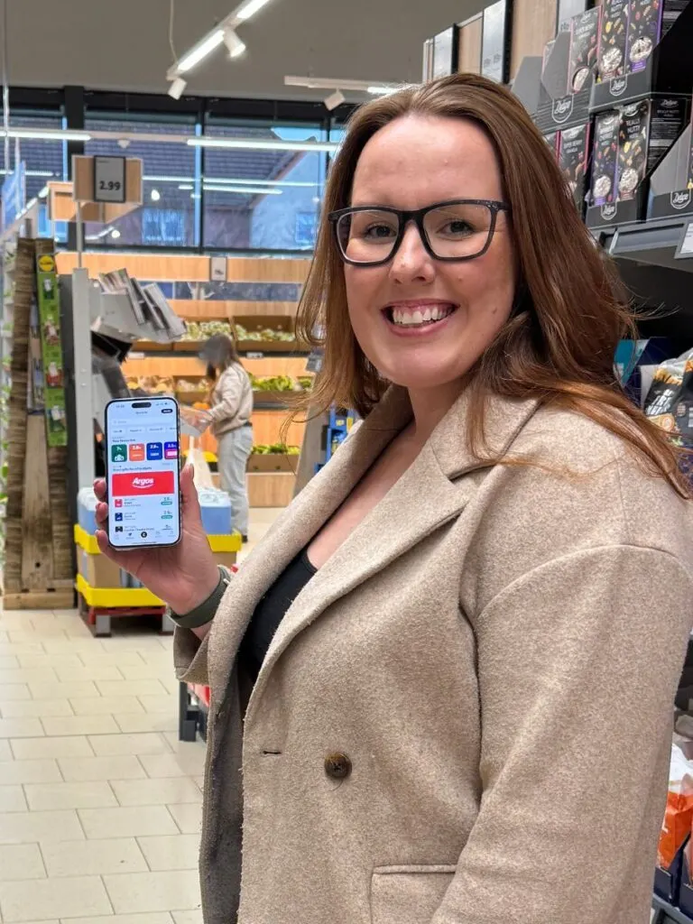 chloe from Chloe's Deal Club in a supermarket holding her phone showing the Cheddar app