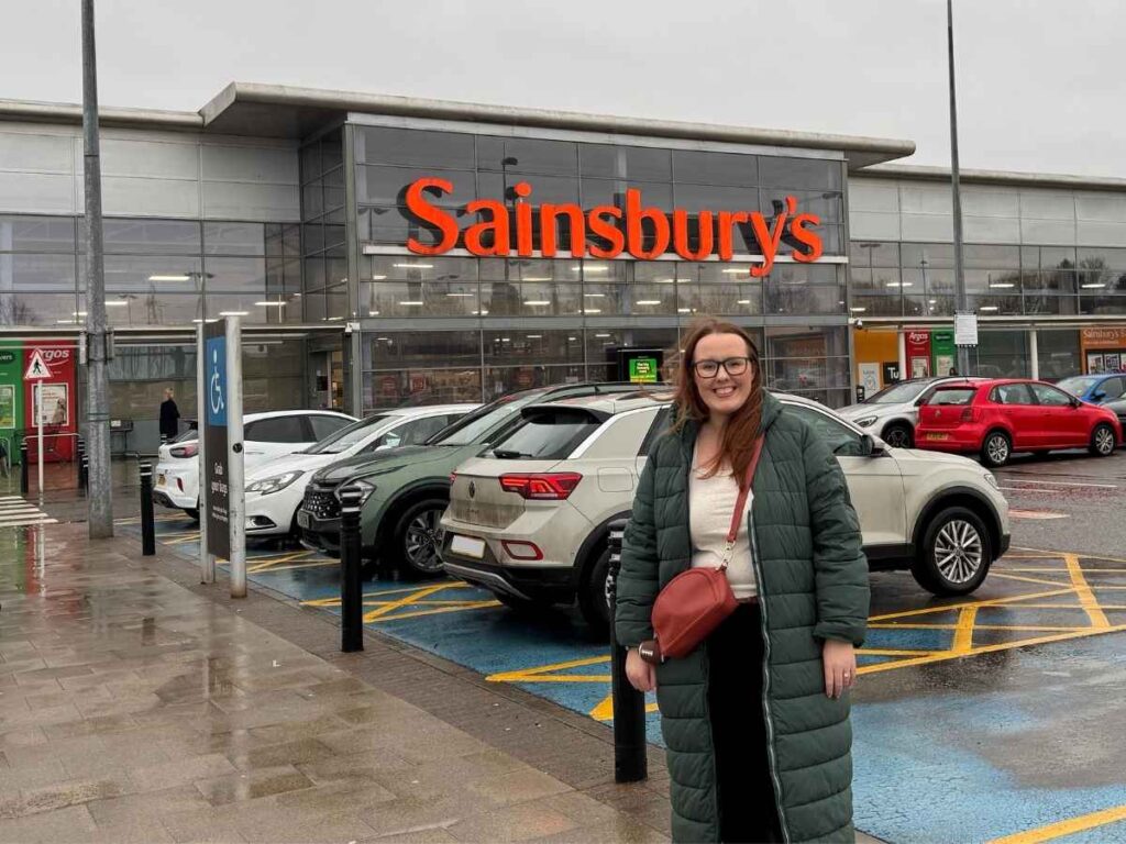 Chloe of Chloe's Deal Club standing in front of Sainsburys showing how to save money when shopping