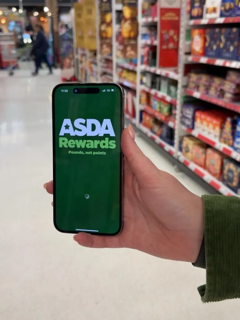 A hand holding a mobile phone with the Asda Rewards app showing on screen to save money at Asda