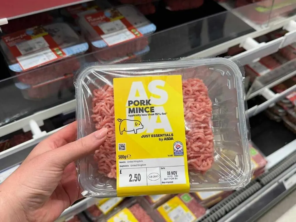 A hand holding Asda just essentials range pork mince to save money at Asda