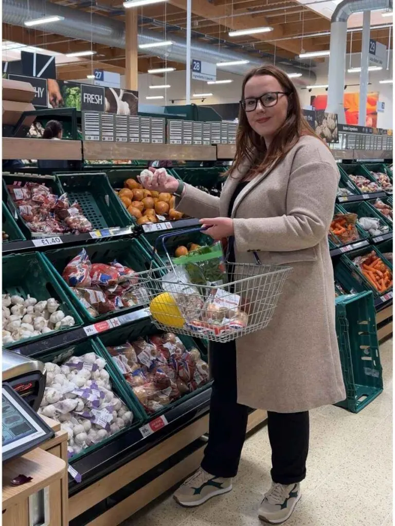 Chloe standing in Tesco supermarket shopping and showing how to save money 