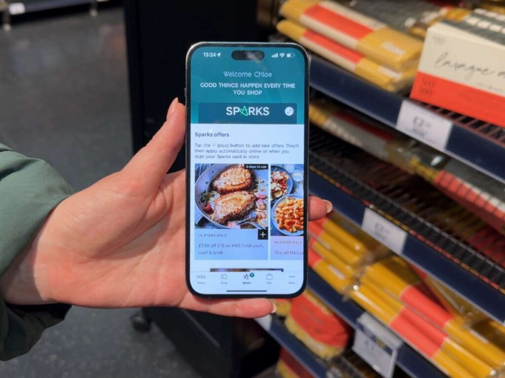 A hand holding a mobile phone displaying the Marks & Spencers loyalty app Sparks with deals to save money