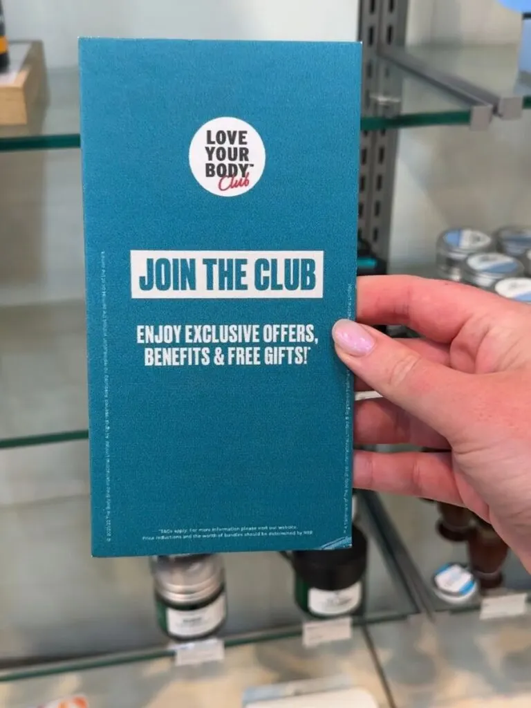 A hand holding a Body Shop sign advertising the Body Club where you can enjoy exclusive offers, benefits and free gifts