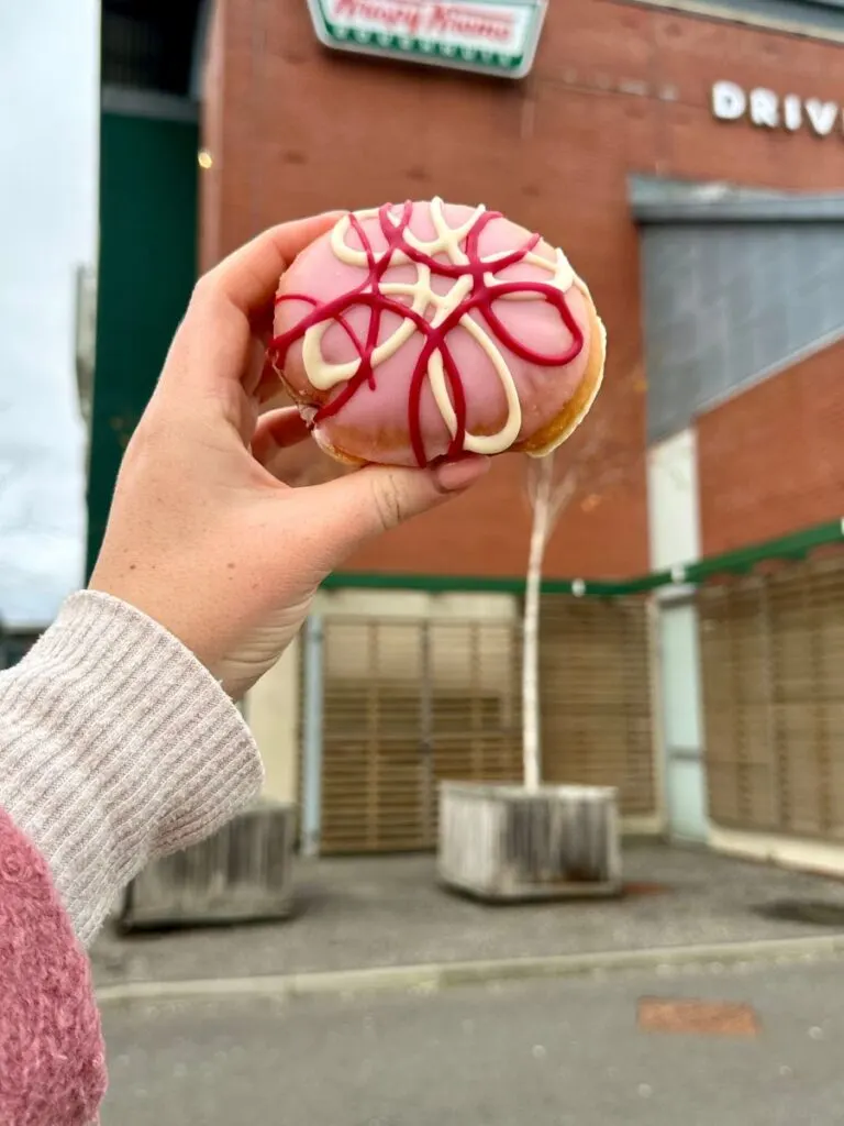 A hand holding a Krispy Kreme pink birthday free doughnut